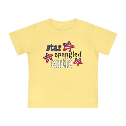 Light yellow Baby t-shrit laying flat with typography and patriotic stars, t-shirt says "star spangled cutie"