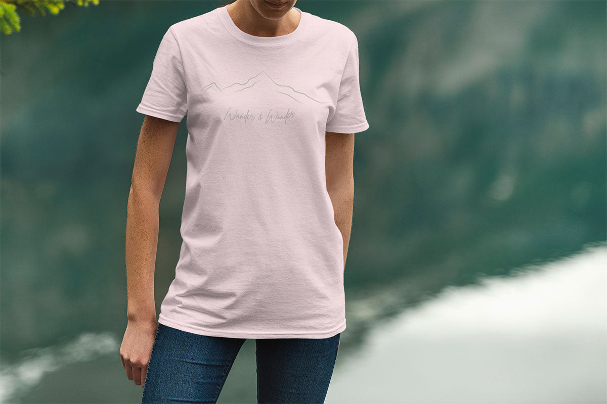 Person standing by lake wearing minimalist unisex mountain t-shirt  for nature lovers in soft pink