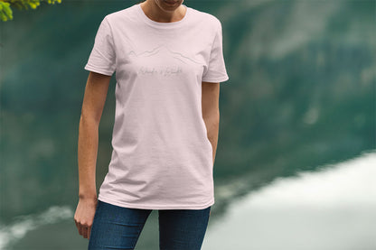 Person standing by lake wearing minimalist unisex mountain t-shirt  for nature lovers in soft pink