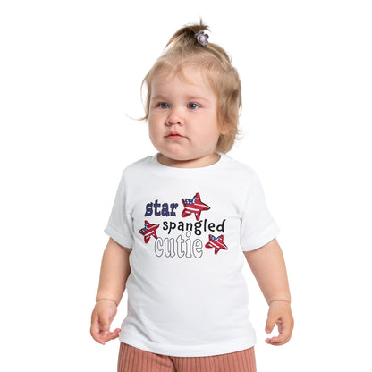 Baby wearing a white t-shrit with typography and patriotic stars, t-shirt says "star spangled cutie"