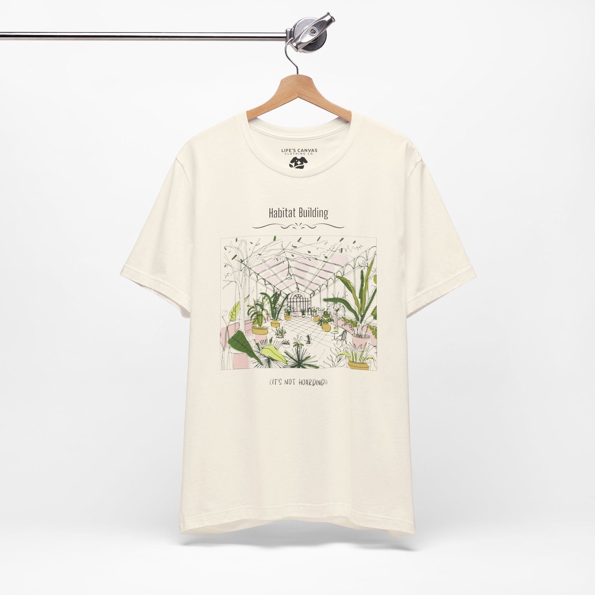 Unisex plant lover shirt that says “Habitat Building, It’s Not Hoarding” on a hanger in Natural