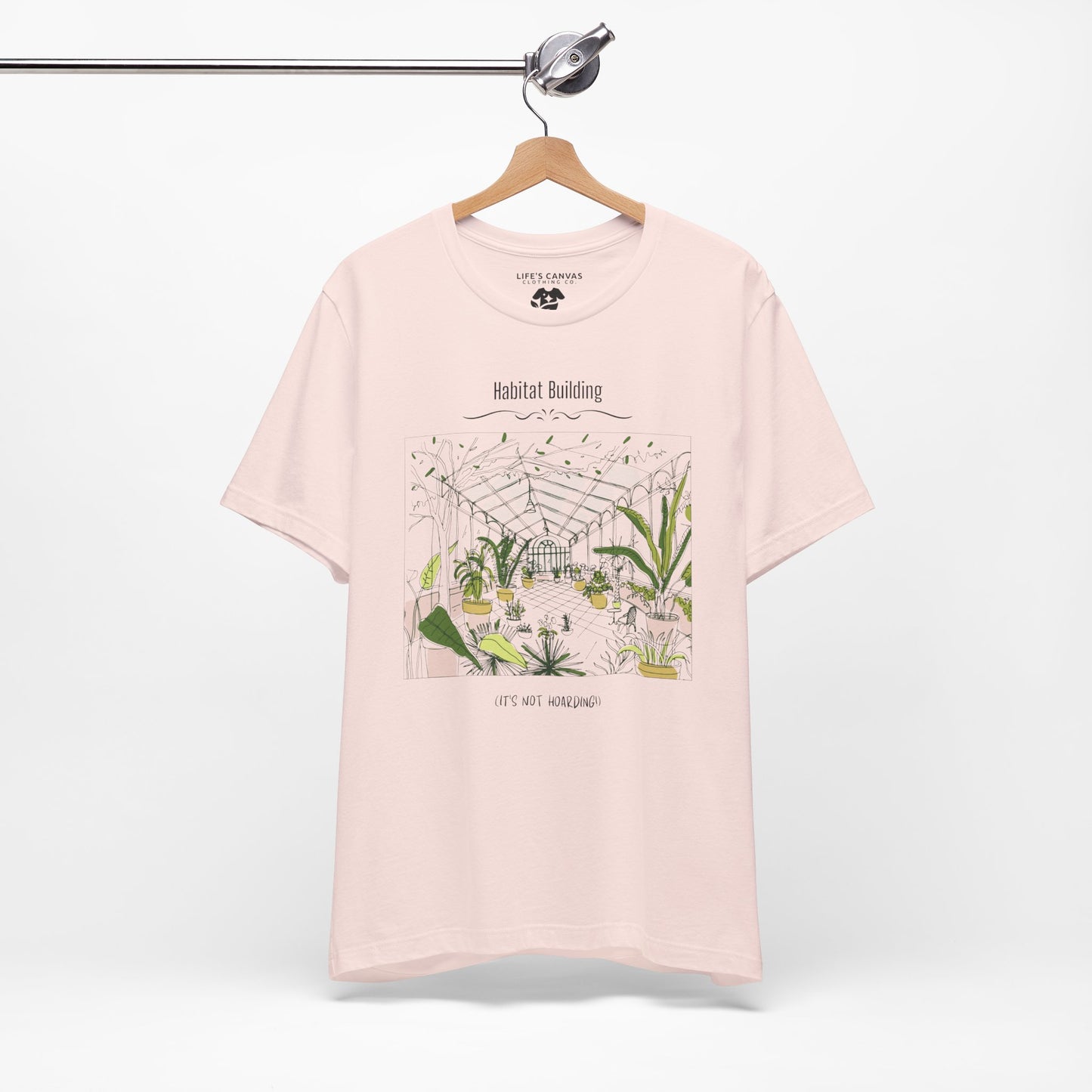 Unisex plant lover shirt that says “Habitat Building, It’s Not Hoarding” on a hanger in Soft Pink