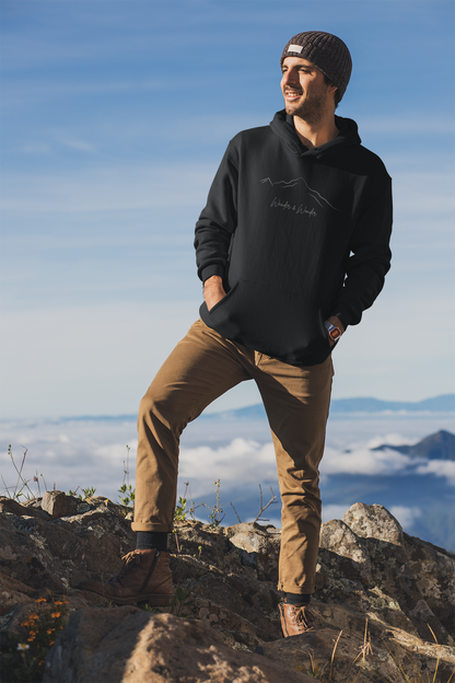 A man standing on a mountain wearing a black hoodies with the text 'Wander and Wonder' on it. 