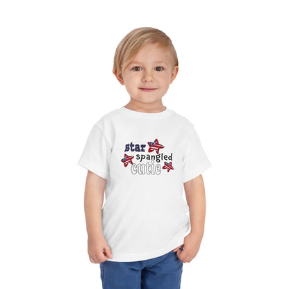 white toddler t-shrit on a model with typography and patriotic stars, t-shirt says "star spangled cutie"