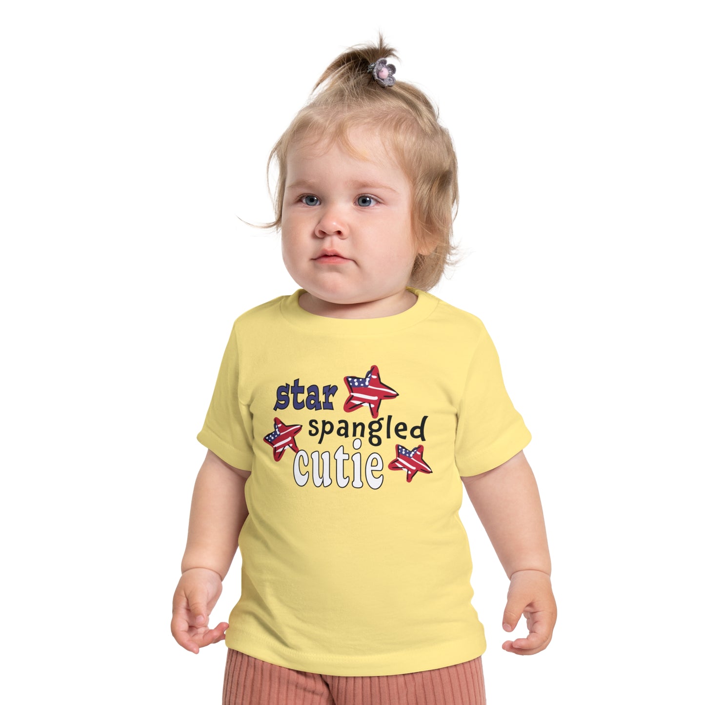 Baby wearing a light yellow t-shrit with typography and patriotic stars, t-shirt says "star spangled cutie"