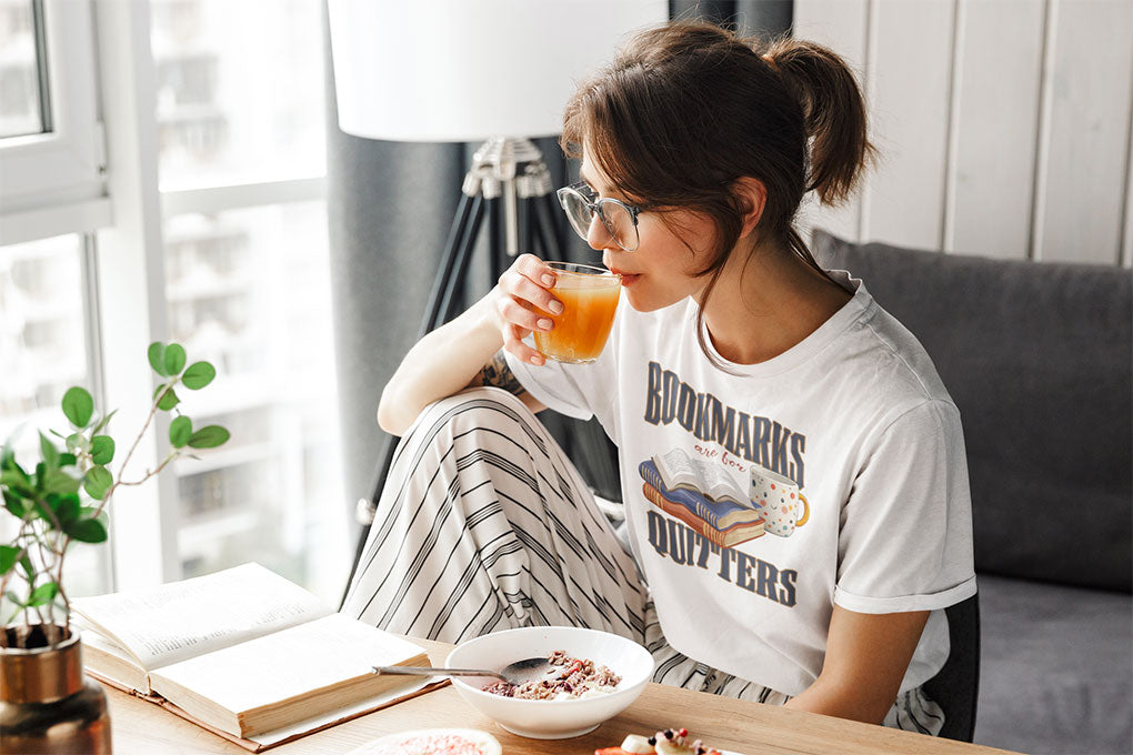 Woman eating breakfast while reading and wearing Bookmarks are for Quitters white t-shirt 