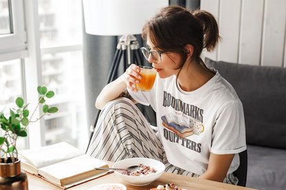 Woman eating breakfast while reading and wearing Bookmarks are for Quitters white t-shirt 